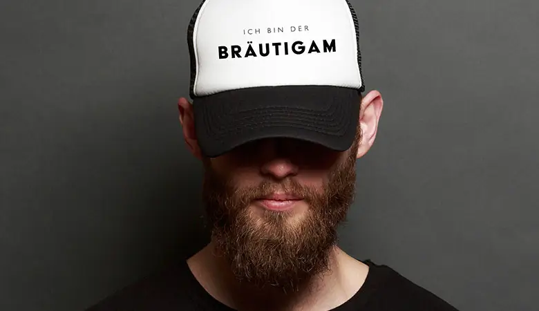 Mann mit schwarzer und weißer Cap mit der Aufschrift „Ich bin der Bräutigam“, ideal für den Junggesellenabschied.