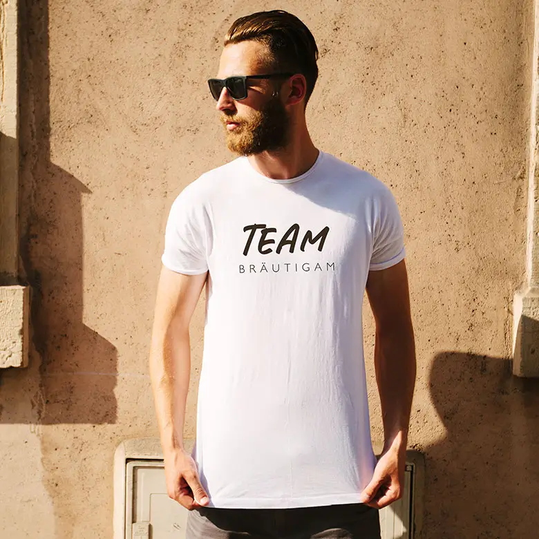 Mann in einem weißen "Team Bräutigam"-T-Shirt, perfekt für den Junggesellenabschied, mit modernem Schriftzug.