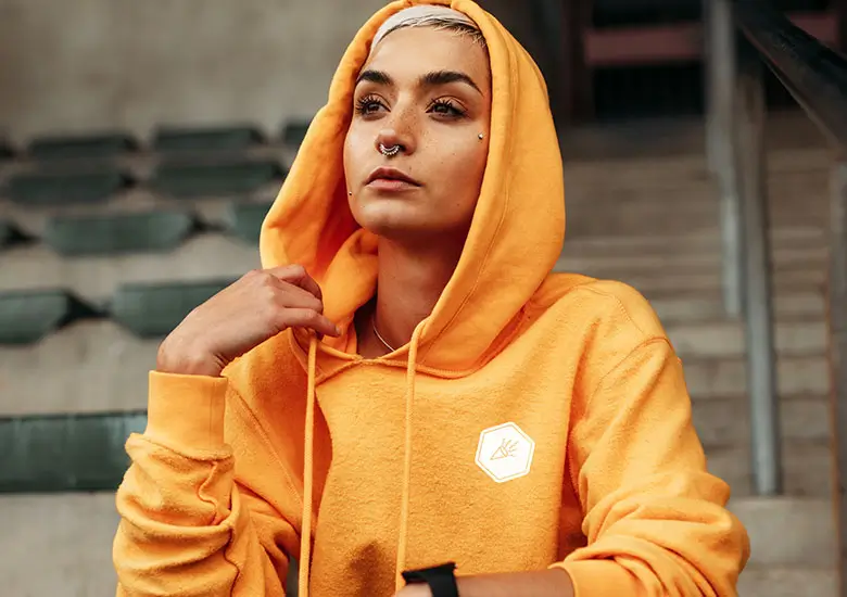 Frau in einem leuchtend orangefarbenen Hoodie mit dezentem, minimalistischem Emblem auf der Brust. Perfekt für moderne Junggesellinnenabschiede.